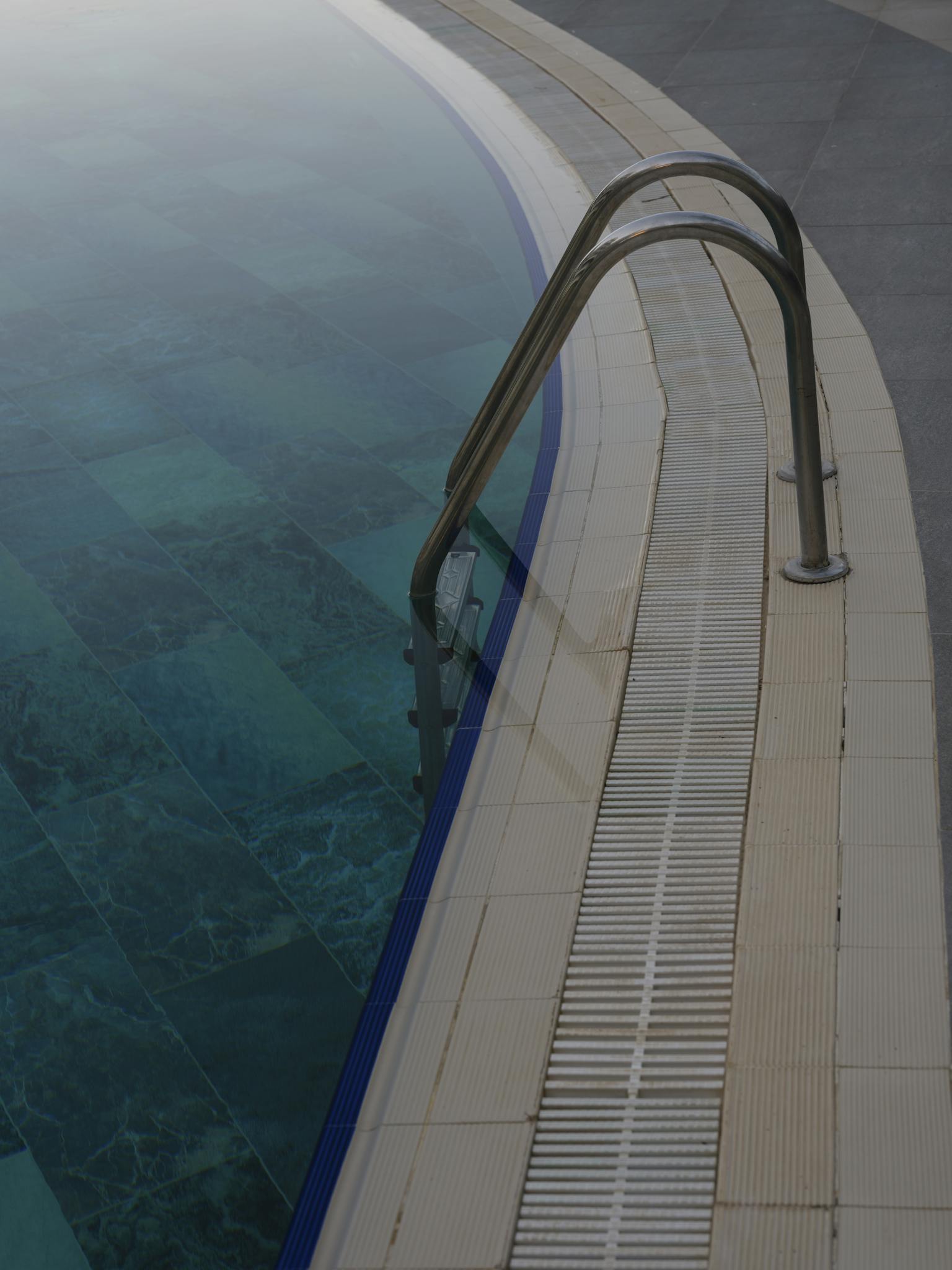 Tranquil swimming pool edge featuring a metal ladder and clear water tiles.